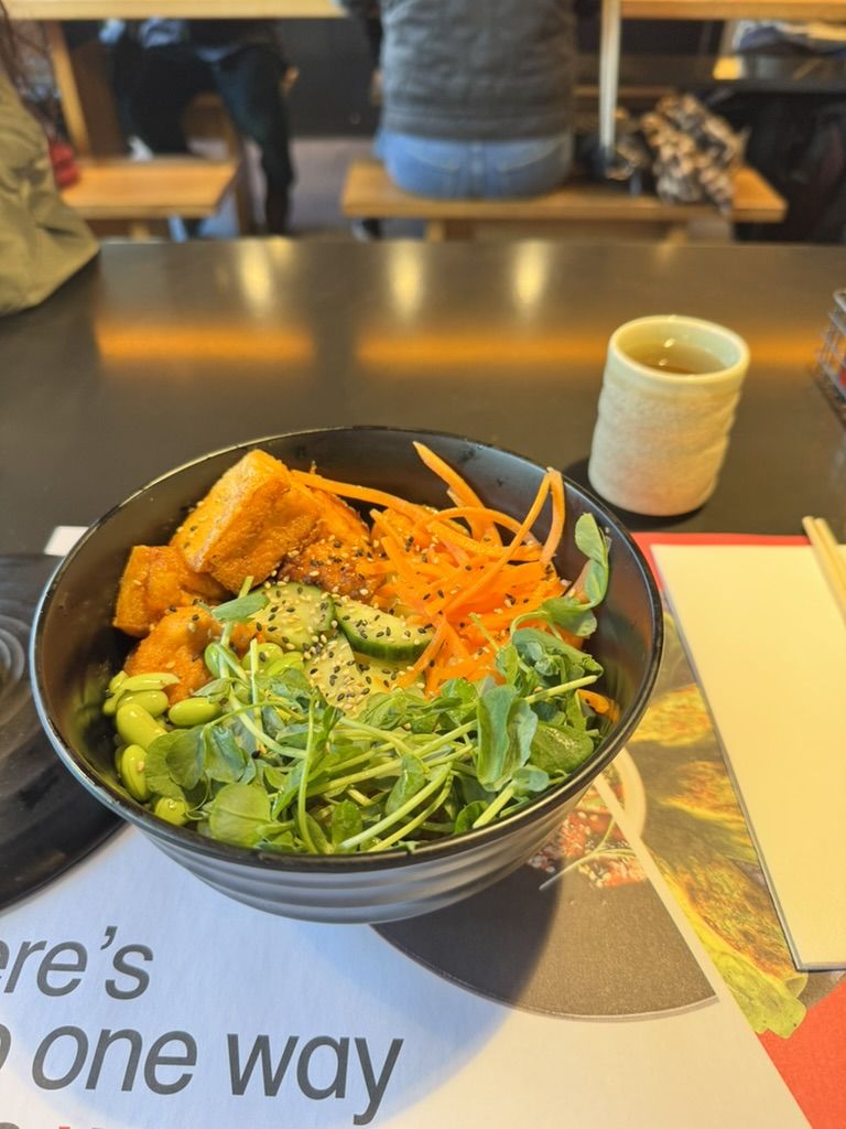A Wagamama donburi rice bowl covered in fresh vegetables and tofu cubes