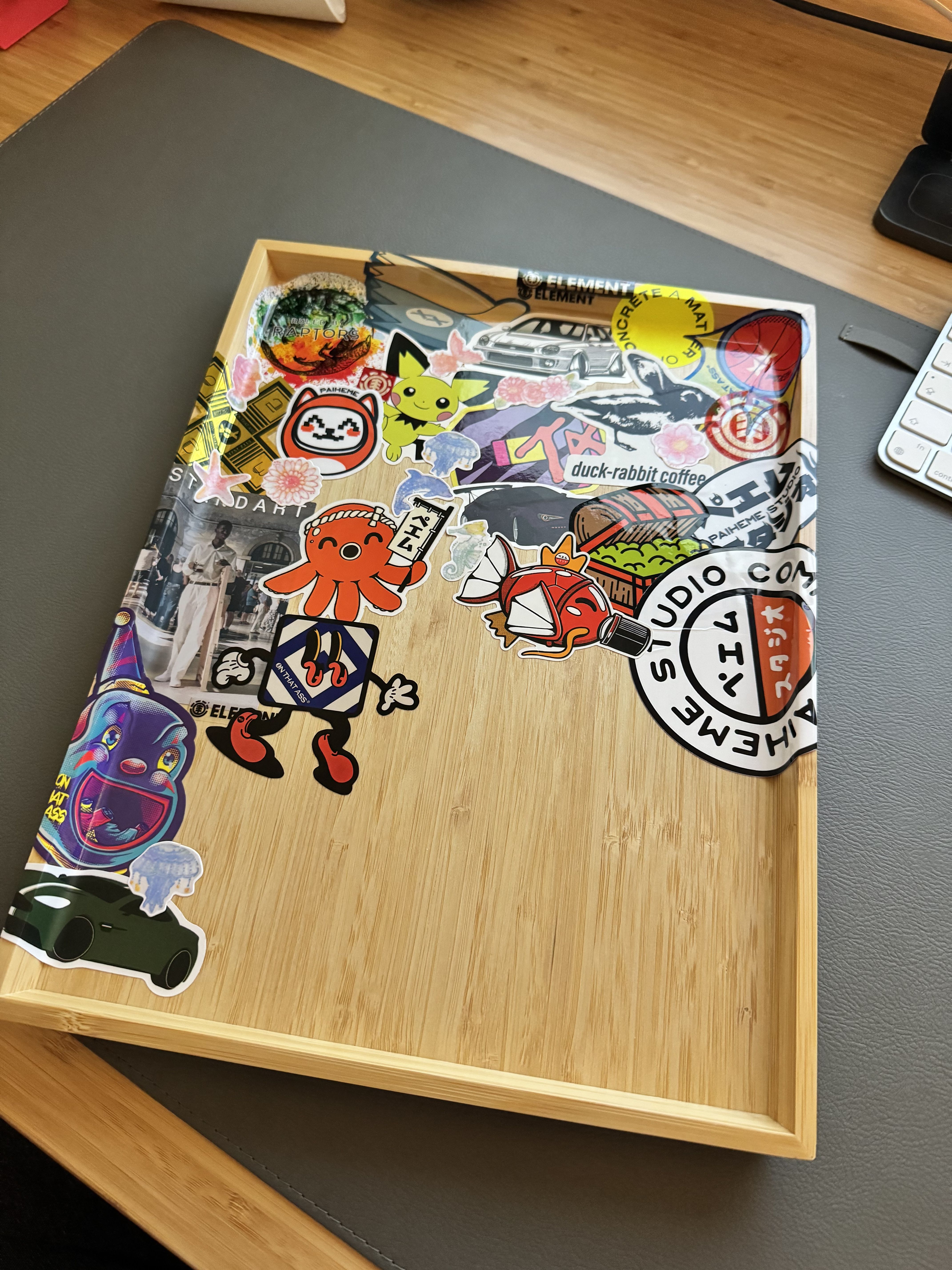 A serving tray half-covered in a variety of stickers including brand logos, cars and Japanese-inspired art
